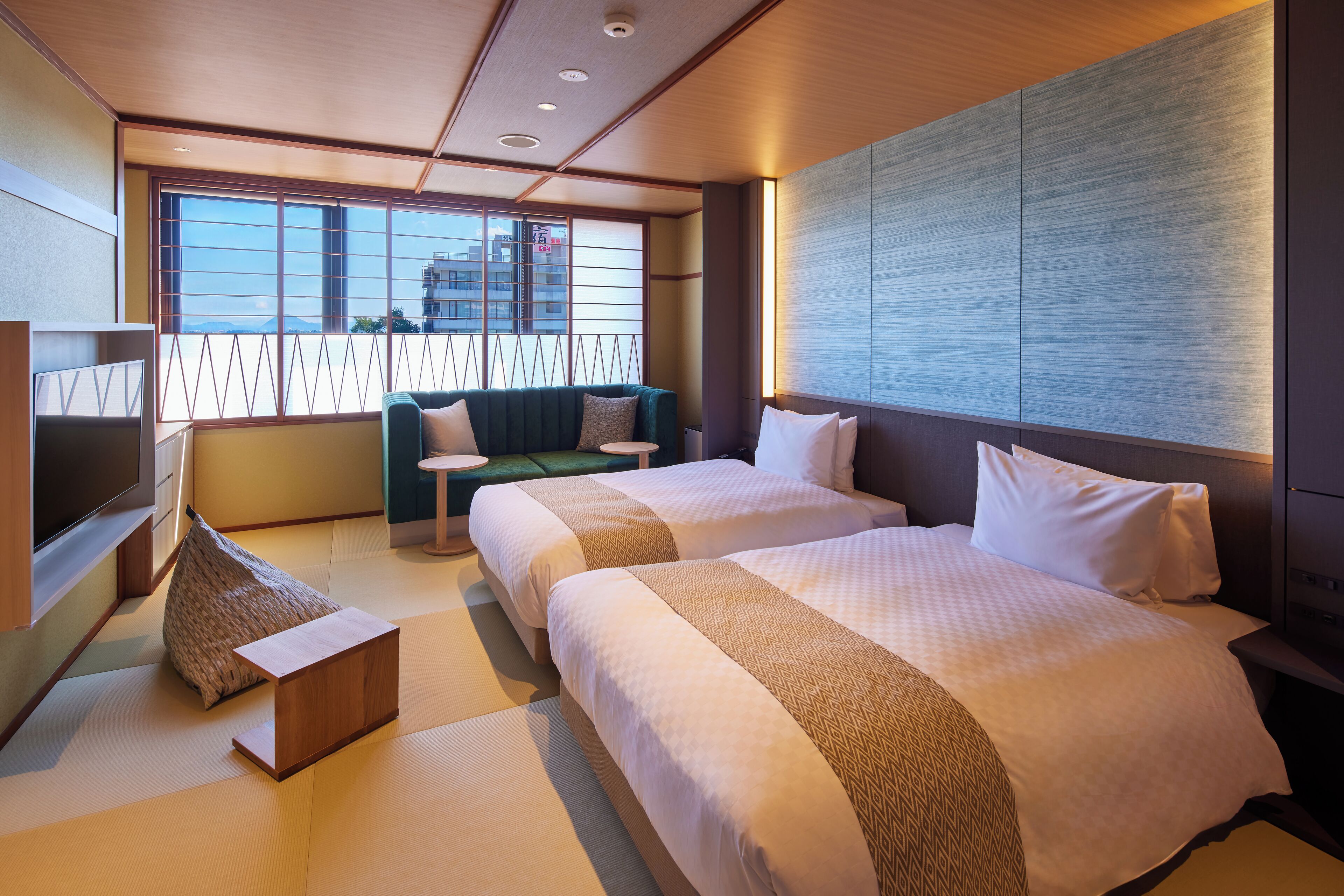 A hotel room with two beds, a sofa, a TV, and a view of the city.