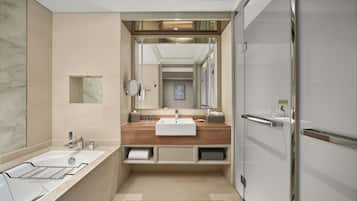 A modern bathroom with a marble wall, a bathtub, a sink with a wooden countertop, and a mirror.