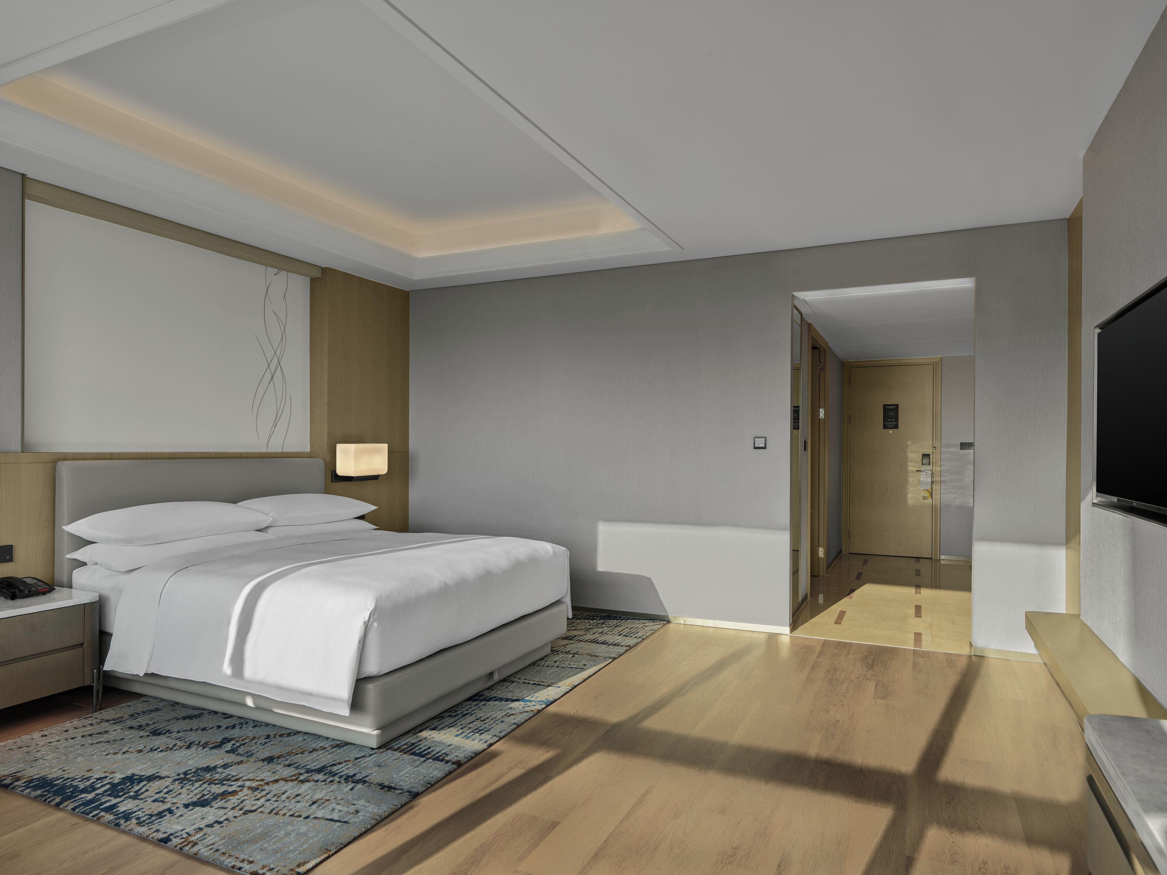 Een moderne hotelkamer met een bed, nachtkastje, lamp en een televisie.