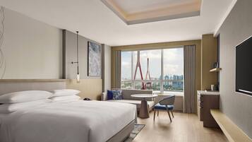 A hotel room with a bed, a desk, a chair, a TV, and a large window with a city view.