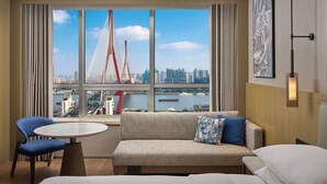A hotel room with a large window, a sofa, a chair, a small table, and a bed. - Shanghai Marriott Hotel Yangpu Riverside (Shanghai)