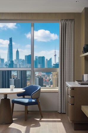 A modern hotel room with a large window offering a city skyline view, a dining area with a table and chair, and a kitchenette. - Shanghai Marriott Hotel Yangpu Riverside (Shanghai)