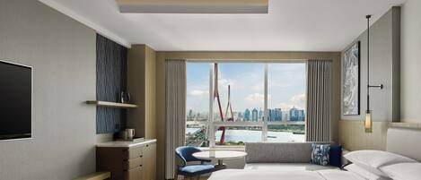 A modern hotel room with a large bed, a desk, a chair, and a TV.
