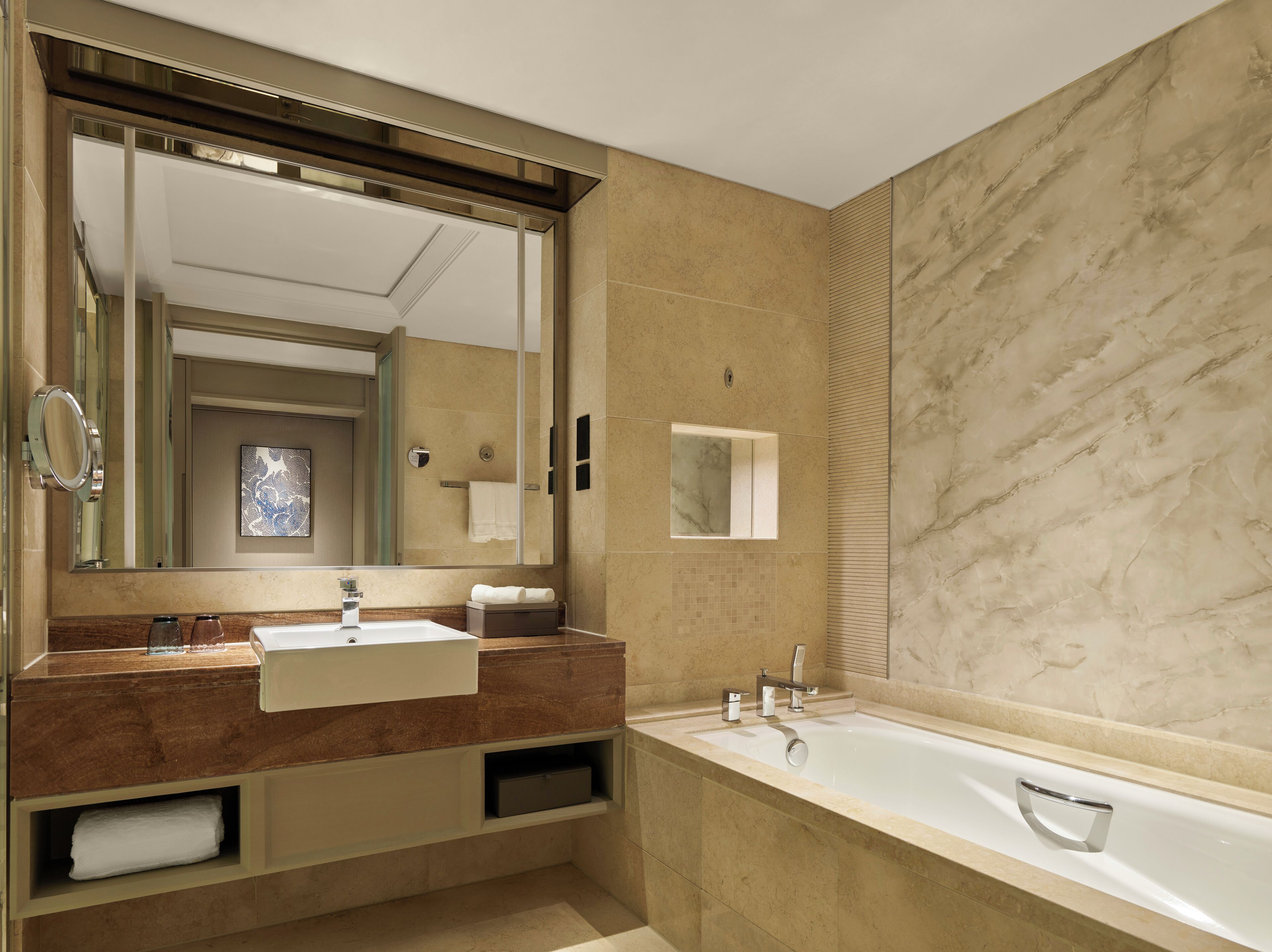 A modern bathroom with a large mirror, two sinks, a bathtub, and a towel rack.