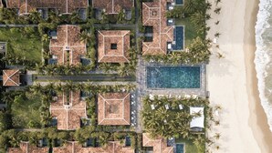 An aerial view of a resort with multiple buildings, a central swimming pool, and a beach. - TIA Wellness Resort - Spa Inclusive (Da Nang)