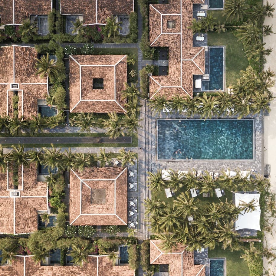 An aerial view of a resort with multiple buildings, a central swimming pool, and a beach.