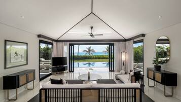 A modern living room with a large TV, a sofa, a coffee table, and a view of a pool and palm trees.