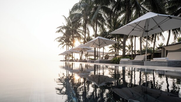 A poolside area with lounge chairs and umbrellas, surrounded by palm trees. - TIA Wellness Resort - Spa Inclusive (Da Nang)