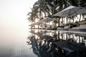 A poolside area with lounge chairs and umbrellas, surrounded by palm trees.