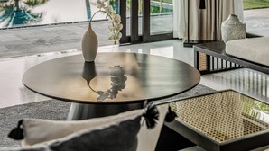 A modern room with a large window, a ceiling fan, a round table, and a view of a pool and palm trees. - TIA Wellness Resort - Spa Inclusive (Da Nang)