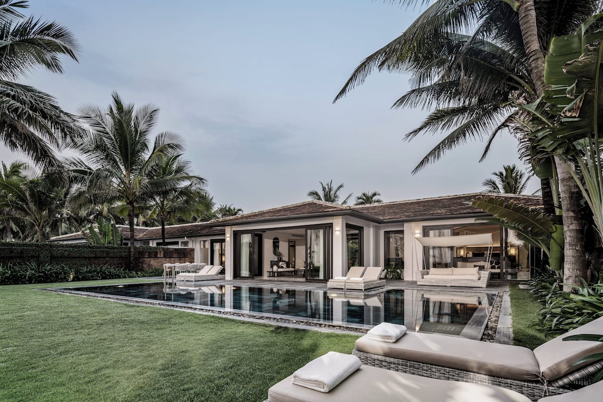 A modern house with a swimming pool, lounge chairs, and palm trees.