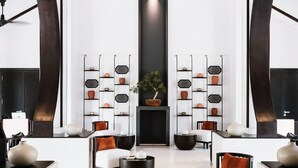 A modern lobby with a central seating area, two tall shelving units with decorative items, and a large black vase on a round table. - TIA Wellness Resort - Spa Inclusive (Da Nang)