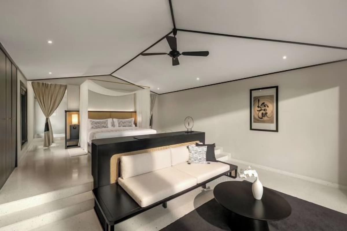 A modern hotel room with a bed, a sofa, a small table, and a ceiling fan.