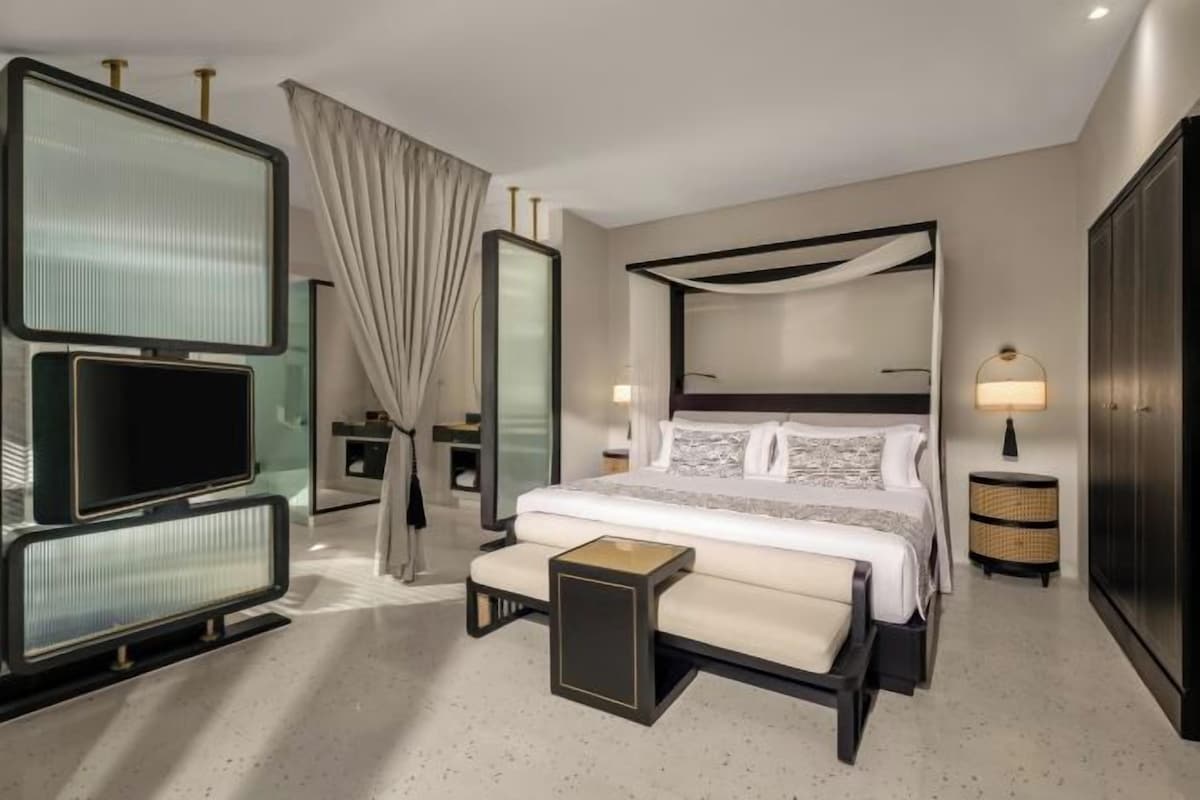 A hotel room with a large bed, a television, a bedside table, a mirror, and a wardrobe.