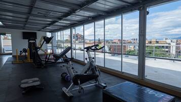 Une salle de sport équipée de matériel d’exercice, dotée de grandes fenêtres et offrant une vue sur le paysage urbain.
