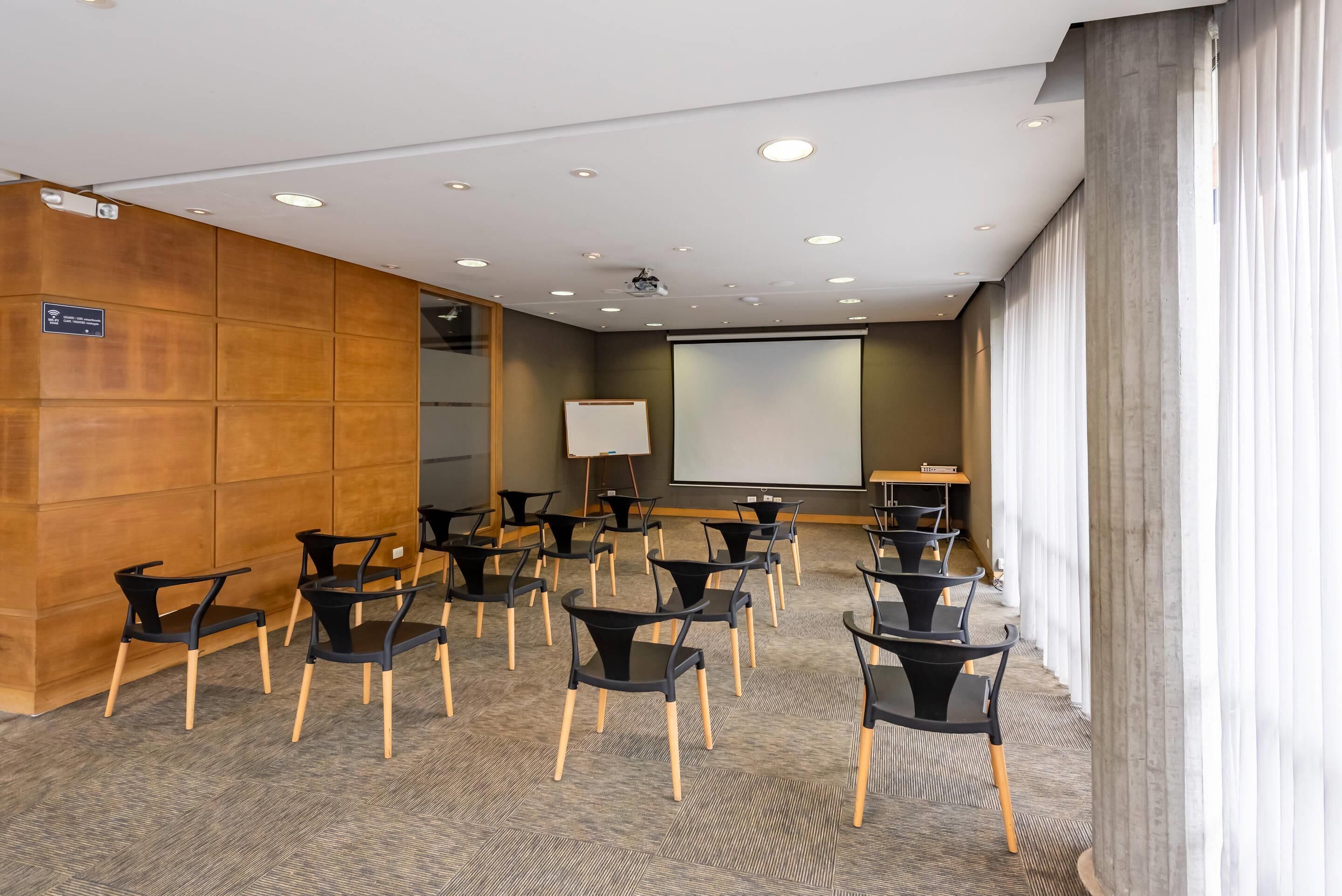 A conference room with a projector screen, multiple rows of chairs, and a large window with curtains.