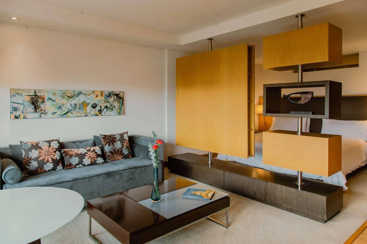 Uma sala de estar moderna com um sofá cinzento, uma mesa de centro, uma estante de livros e um quadro na parede.