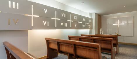 Interior de una iglesia moderna con bancas de madera y una pared mostrando números romanos.