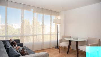 A modern living room with a sofa, two chairs, a small table, and a floor lamp. Large windows provide a view of the outside.