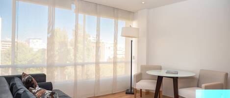 Una sala moderna con un sofá, dos sillones, una mesita y una lámpara de pie. Amplias ventanas ofrecen vistas al exterior.