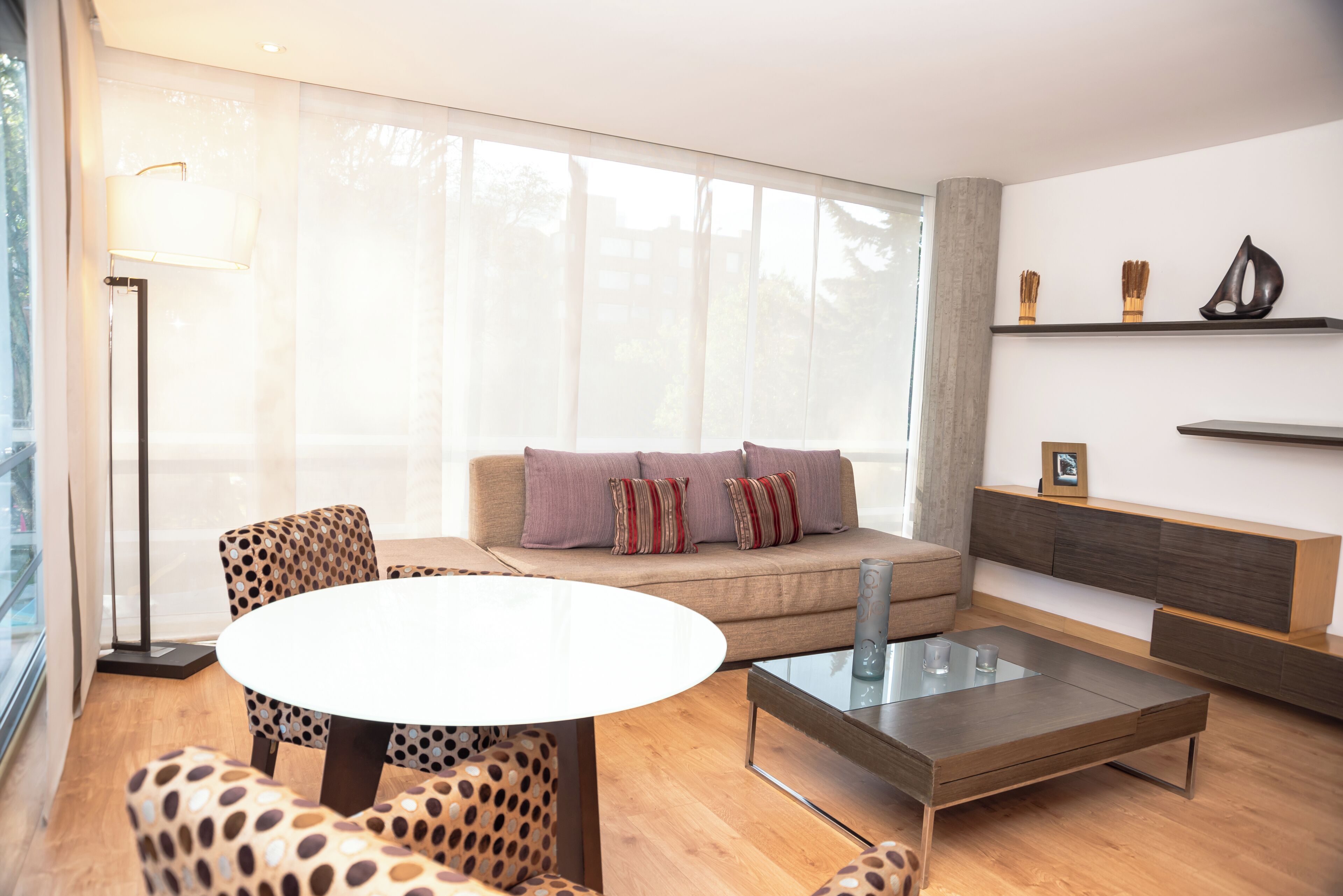 A modern living room with a sofa, a glass coffee table, and patterned chairs.