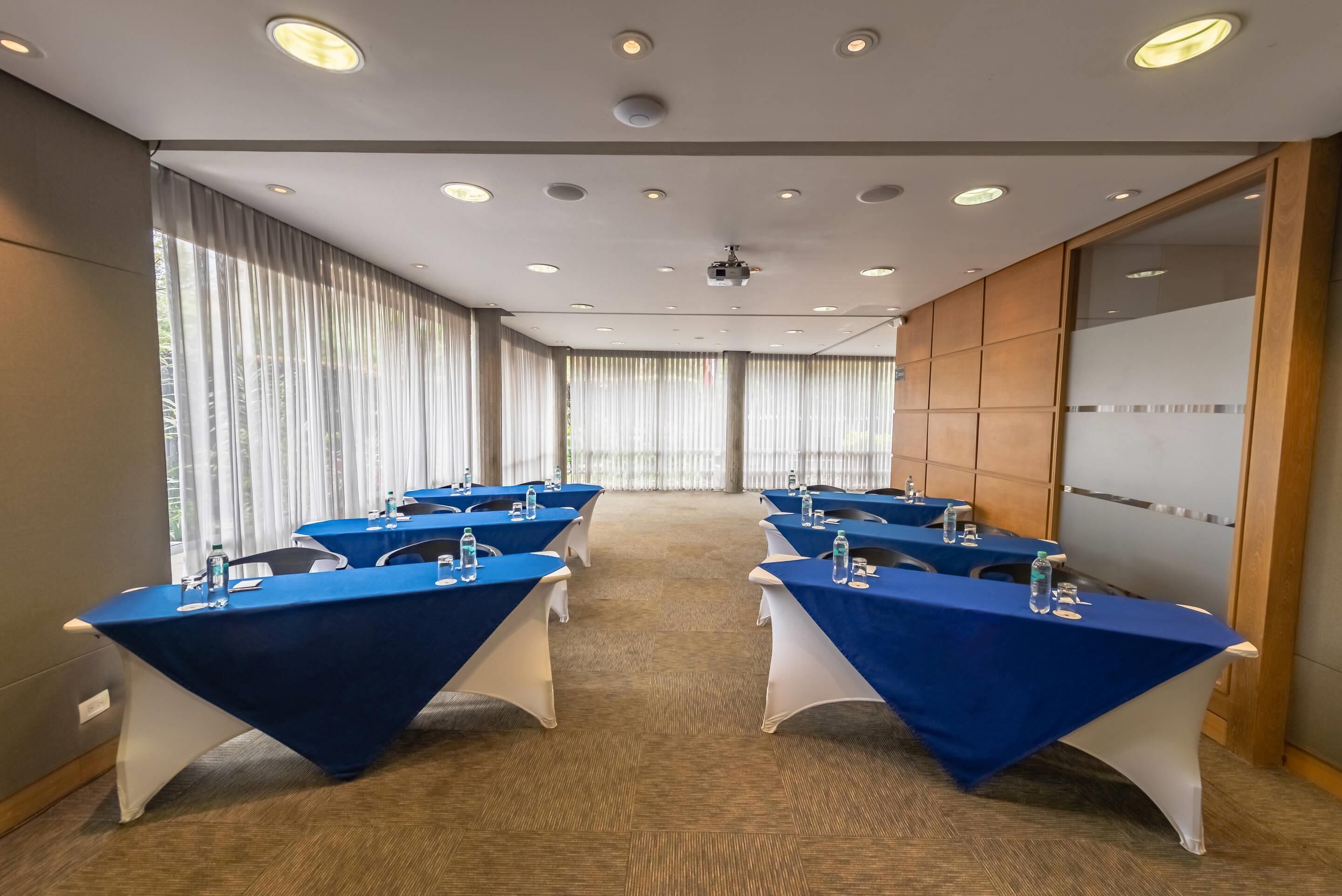 Un salón de conferencias con mesas, sillas y un proyector.