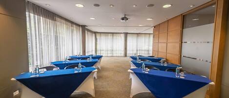 Un salón de conferencias con mesas, sillas y un proyector.