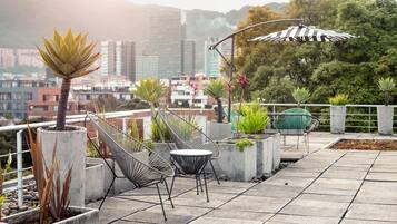 A rooftop terrace with seating, potted plants, and a cityscape view.