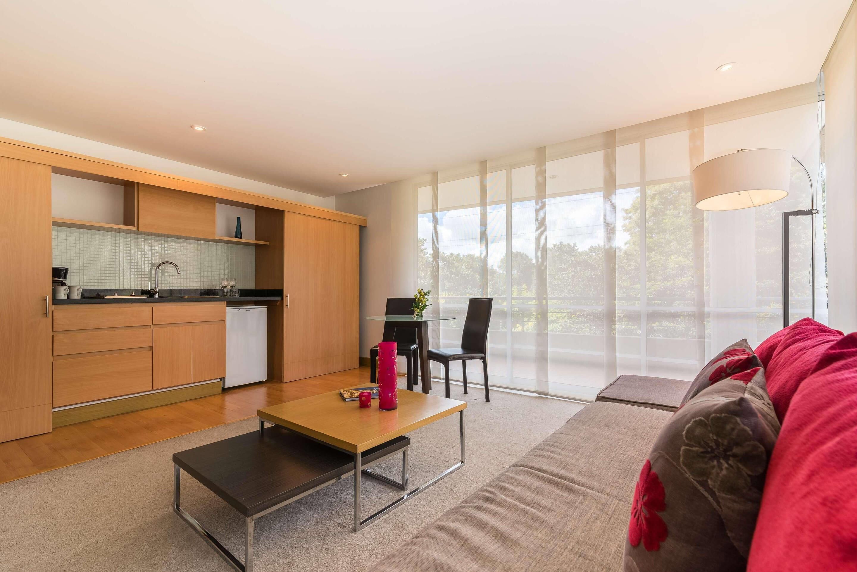 A modern kitchen with wooden cabinets, a dining area with a table and chairs, and a large window providing natural light.