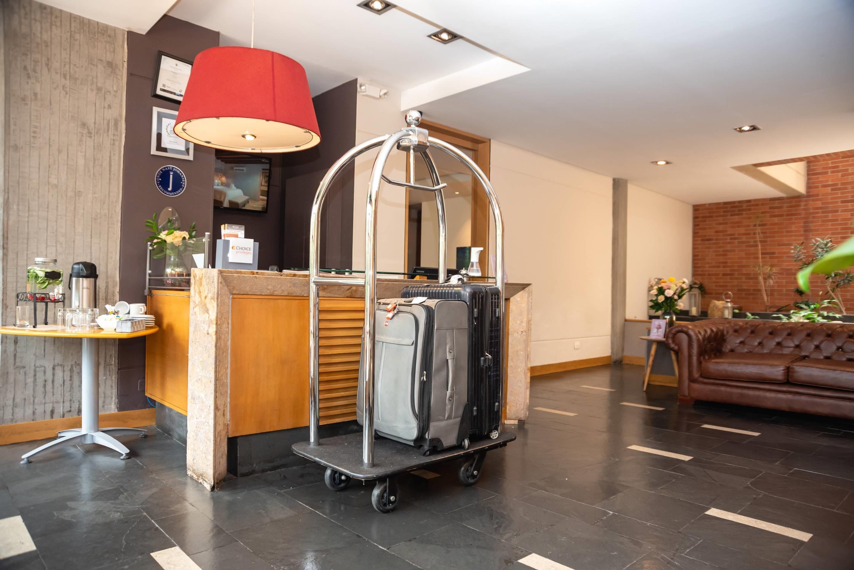 A reception area with a desk, a cart with luggage, a red lamp, and a brown leather sofa.