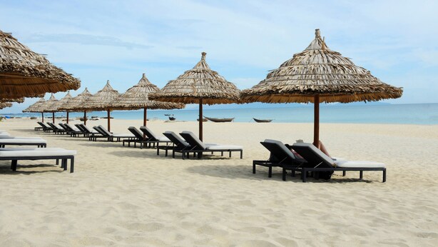 A beach with rows of sun loungers and thatched umbrellas.