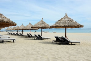 Ein Strand mit Reihen von Liegestühlen und reetgedeckten Sonnenschirmen.