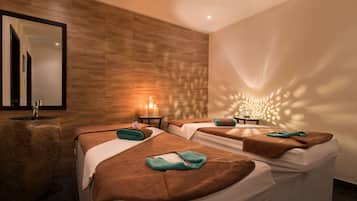 Relax in a serene spa room with two massage beds, each with a small table for personal items, and a large mirror above.