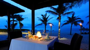 A table set for dining with a view of the beach and palm trees at dusk.