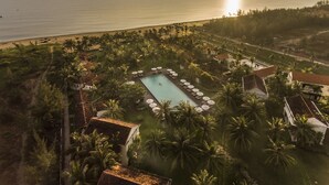 A resort with a swimming pool surrounded by palm trees and a view of the ocean. - Boutique Hoi An Resort (Da Nang)