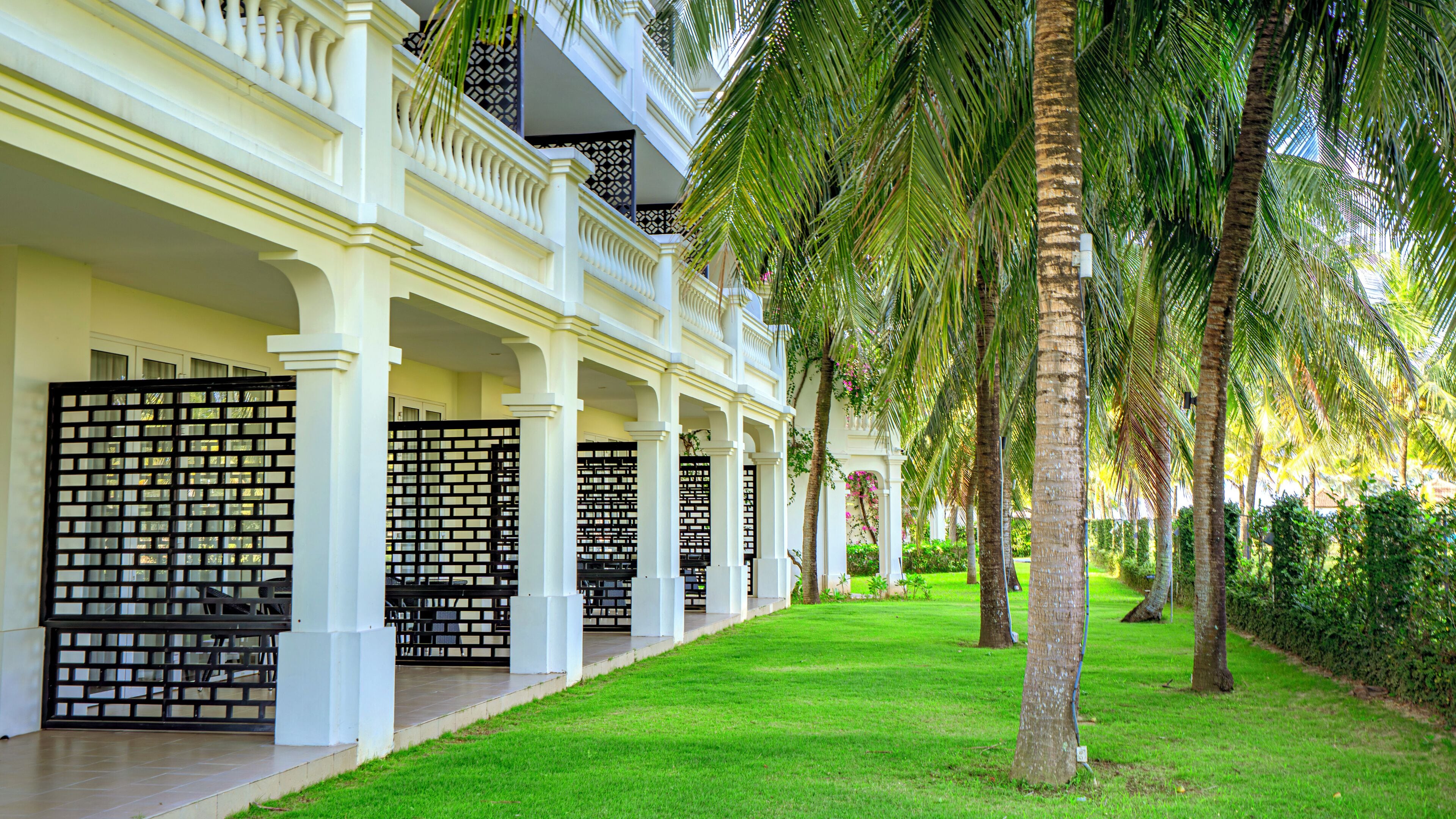 A hotel with a covered walkway, palm trees, and a well-maintained lawn.