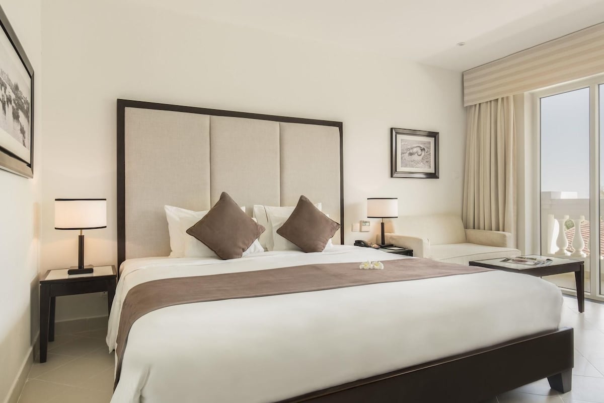 A hotel room with a large bed, two bedside tables, a sofa, and a view of the outdoors.