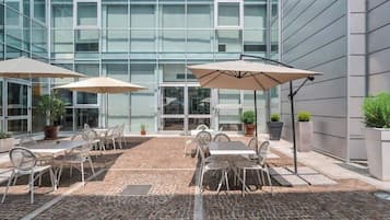 Un patio al aire libre con mesas, sillas, plantas en macetas y sombrillas.