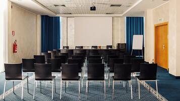 A conference room with rows of chairs, a projector screen, a whiteboard, and a fire extinguisher.