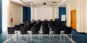 A conference room with rows of chairs, a projector screen, a whiteboard, and a fire extinguisher. - Park Hotel Cassano (Cassano d'Adda)