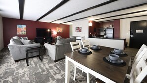 Una sala moderna con sofá, sillas, una mesita de centro y una mesa de comedor con tazones. Se ve una cocina al fondo, con microondas y refrigerador.