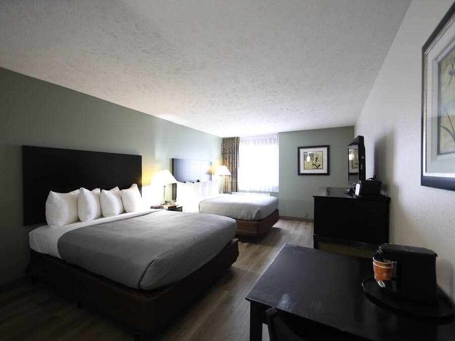 Una habitación de hotel con una cama grande, una cama más pequeña, un escritorio con cafetera y una cómoda.