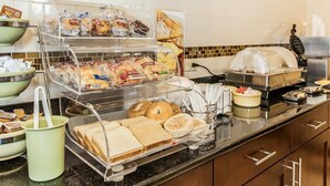Zona de bufé con diversas opciones de comida, incluyendo panes, pasteles y una estación de alimentos calientes.