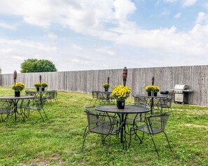 A backyard with multiple round metal tables and chairs, surrounded by a wooden fence.