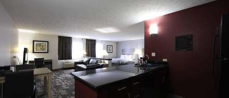 A hotel room with a kitchenette, a dining area, a bed, and a bathroom.