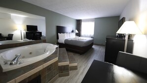 Habitación de hotel con una bañera grande, cama con ropa blanca, televisor de pantalla plana y escritorio con lámpara.