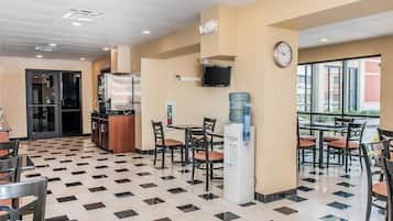 Un hall d’hôtel avec un sol à carreaux, un distributeur d’eau, une horloge et un téléviseur fixé au mur.