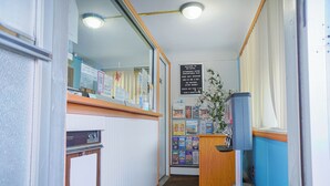 A narrow hallway with a reception desk, a bulletin board with various notices, and a trash can.