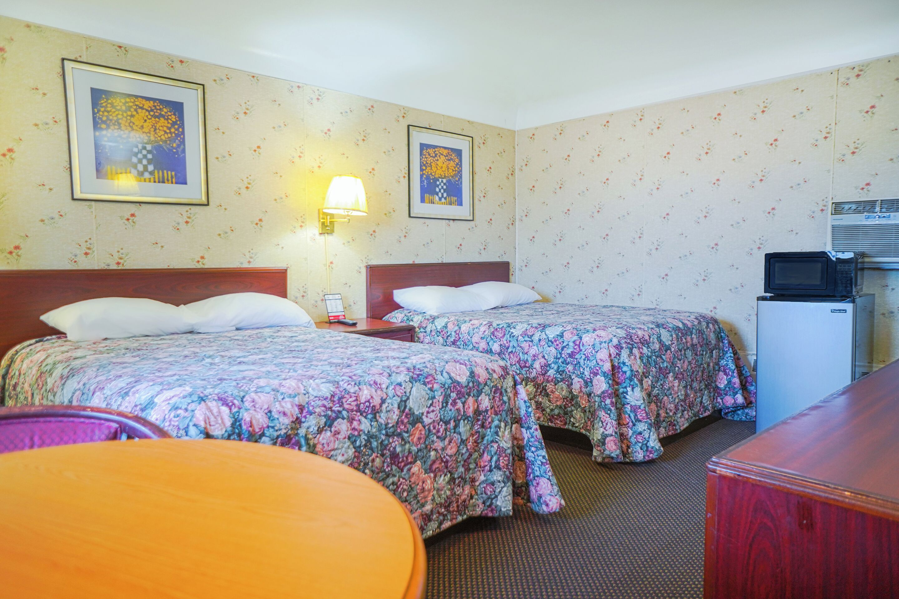 Hotellihuone, jossa on kaksi sänkyä, työpöytä, tuoli, lamppu ja mikroaaltouuni.
