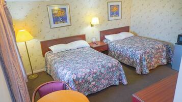 A hotel room with two beds, a desk, a chair, a lamp, and a television.